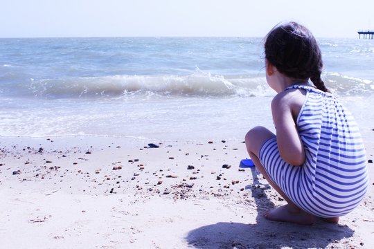 Girl (4-5) crouching on beach