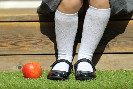 Close-up of a young schoolgirl in knee high socks sitting on a step with apple on the grass by her feet
