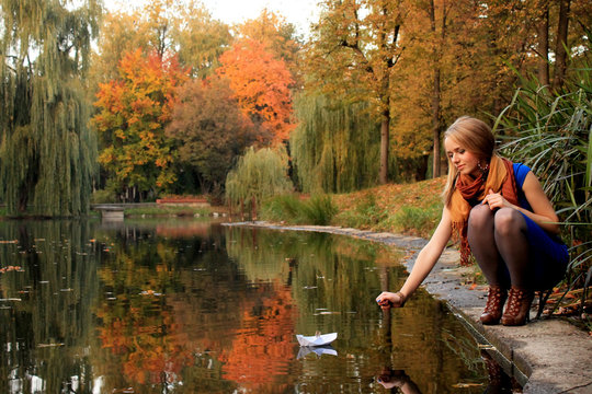 Young woman crouching by a lake pushing a paper boat with a twig