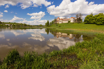 Fototapeta na wymiar old castle and green reflection in blue water with cloudy sky background