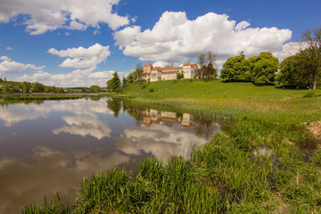 Fototapeta na wymiar old castle and green reflection in blue water with cloudy sky background