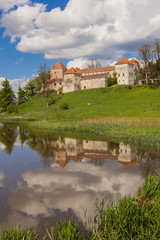 old castle and green reflection in blue water with cloudy sky background