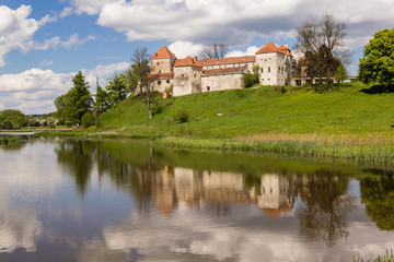 Fototapeta premium old castle and green reflection in blue water with cloudy sky background