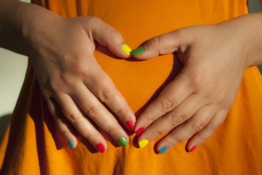 Close-up Mid-section view of woman with multi coloured nail polish making a heart shape with her hands in front of her stomach 