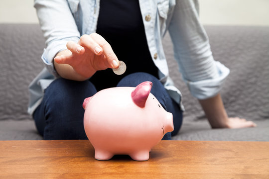 Close-up of a woman sitting on a sofa inserting a coin into a piggy bank