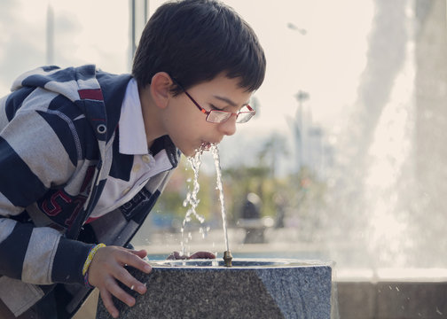 Close-up side view of a Teenage boy drinking water from a water fountain in the park, Cordoba, Spain