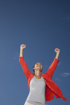 Woman with raised arms against blue sky