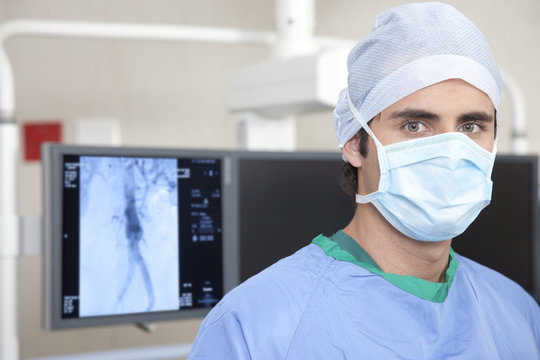 Portrait of a surgeon wearing a protective face mask standing in an operating theatre in front of a CT scanner