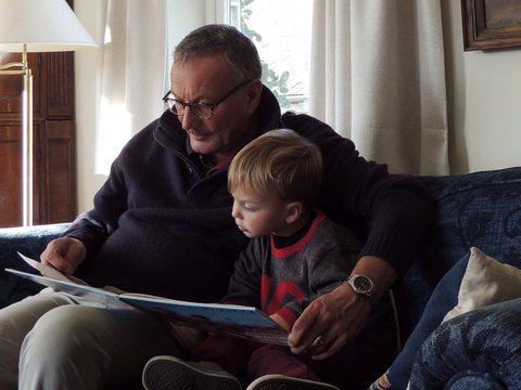 Grandfather and grandson reading book while sitting on sofa at home