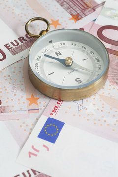 Close-up of a compass on top of Euro banknotes