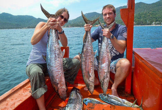 Smiling Man and woman sitting in a boat with freshly caught mahi mahi and mackerel, Koh Tao, Thailand