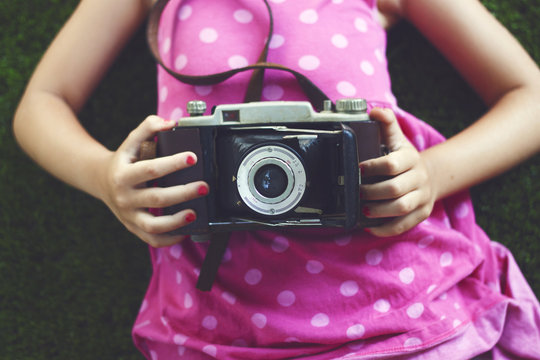 Close-up mid section of a Girl in a pink polka dot dress and nail polish holding a vintage camera