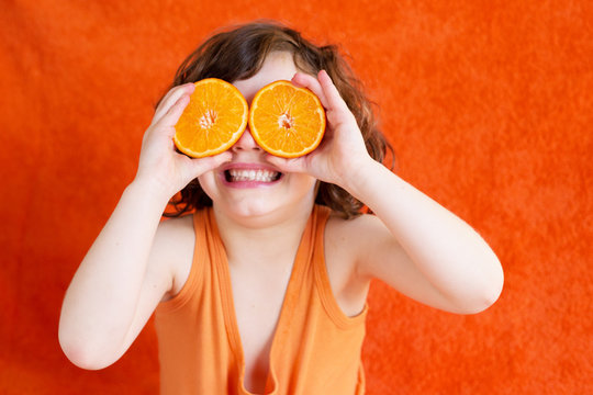 Smiling Girl dressed in orange holding halved oranges in front of her eyes