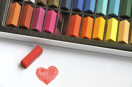 Red crayon next to a Heart drawn on a piece of paper and a box of assorted colourful crayons