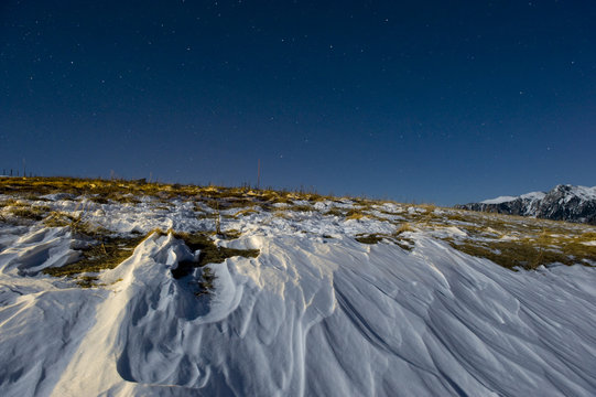 Snow sculpted by wind in a moonlit mountain scene at night.