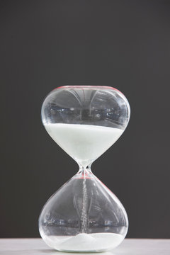 Close-up of a glass hourglass sand timer on a table with a black background