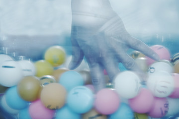 Close-up of a hand picking a plastic lottery ball from glass bowl