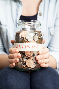 Full frame close-up of a Woman sitting on a chair holding a glass savings jar filled with coins