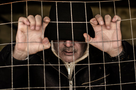 Close-up of a man in a beanie hat trapped and holding onto a metal fence