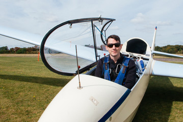 Smiling man wearing sunglasses sitting in an open glider at an airfield before take off, England, UK
