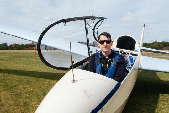 Smiling man wearing sunglasses sitting in an open glider at an airfield before take off, England, UK