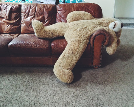 Naklejki Oversized stuffed teddy bear lying on the edge of a sofa in a living room 