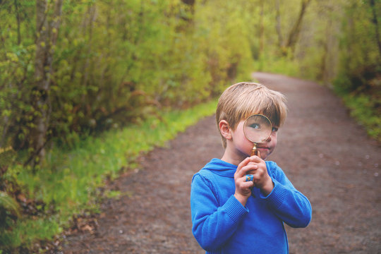 Boy (4-5) looking through magnifying glass on nature trail