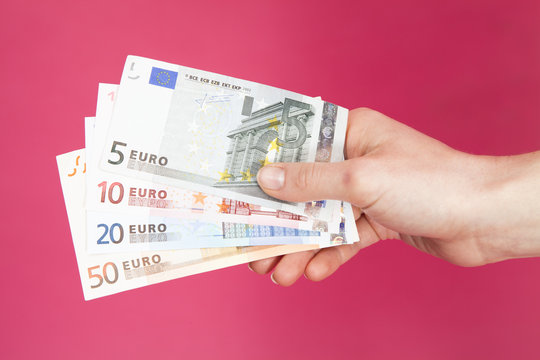 Close-up of a Hand holding a fan of assorted euro bank notes in front of a pink background