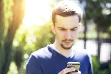 Fototapeta premium Young man using smartphone outdoors in bright sunlight