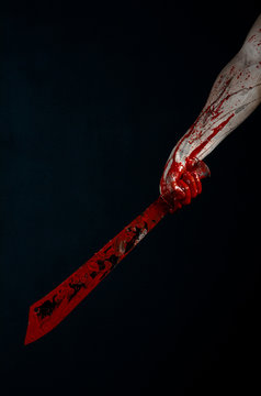 bloody hands holding a bloody machete isolated in studio