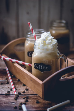 Close-up of two coffees with whipped cream in mason jars on a tray with chocolate chips on a table