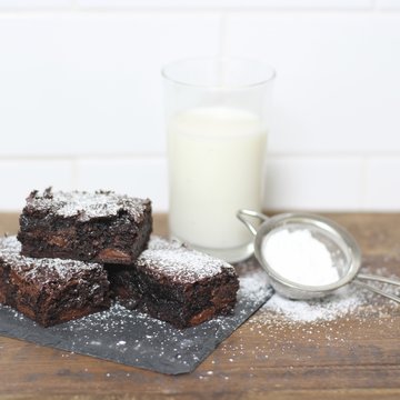 Chocolate brownies dusted with icing sugar and a glass of milk on a  table