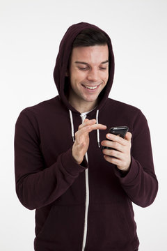 Smiling man in a hoodie standing in front of a white background using  a mobile phone