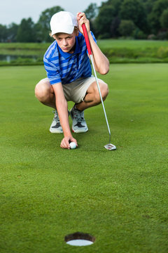 Teenage boy placing golf ball on golf course
