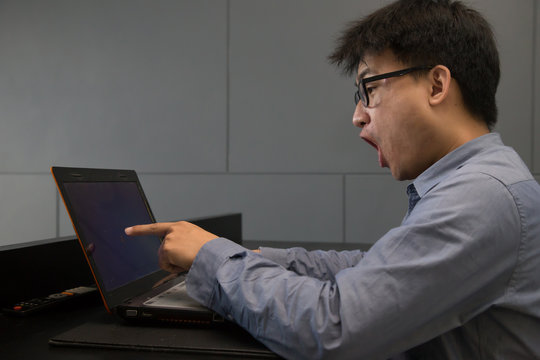 Asian man surprised with laptop computer looking at screen excit