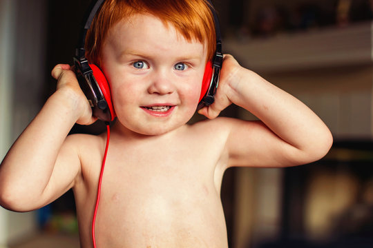 Portrait of a smiling shirtless Boy standing in a living room wearing headphones listening to music 