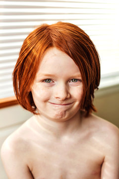 Portrait of smiling shirtless boy sitting in front of a window
