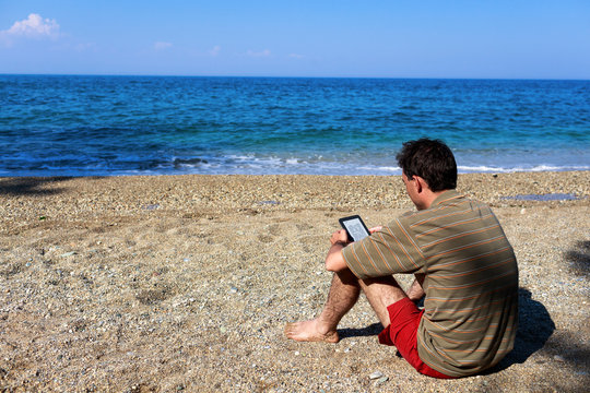 Greece, Thessaloniki, Man reading e-reader on beach