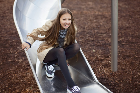 Happy teenage girl messing about on a slide in a playground