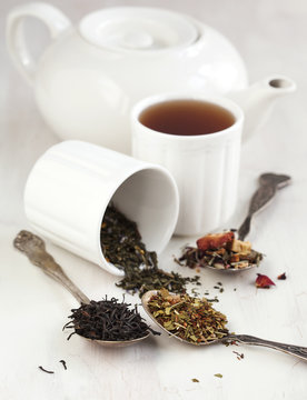 Close-up of a teapot and two mugs with assorted spoonfuls of loose leaf tea on a table 