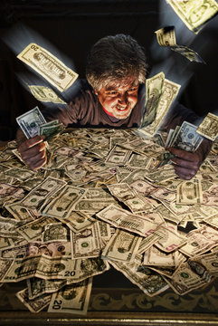Greedy man sitting in front of a stack of money throwing dollar bills in the air