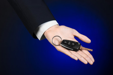 car salesman in a black suit holds the keys to a new car studio