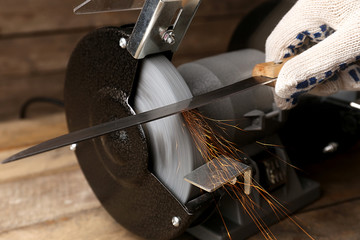 Knife sharpener and hand with blade on wooden table, closeup