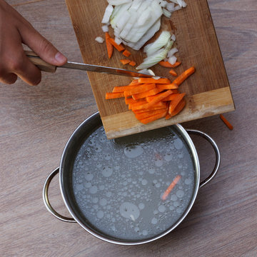 Female hands putting vegetables ingredients into chicken soup