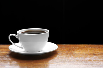 Cup of coffee on wooden table on black background