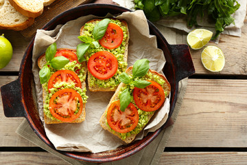 Vegan sandwich with avocado and vegetables on pan, on wooden background