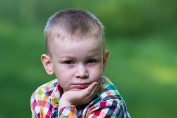 A little boy sitting on the grass and looking thoughtfully ahead