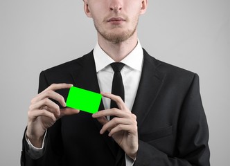 businessman in a black suit and black tie holding a green card