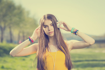 Beautiful teenage girl listening to music on headphones in park