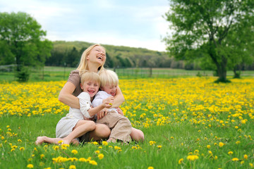 Mother and Young Children Sitting in Flower Meadow Laughing